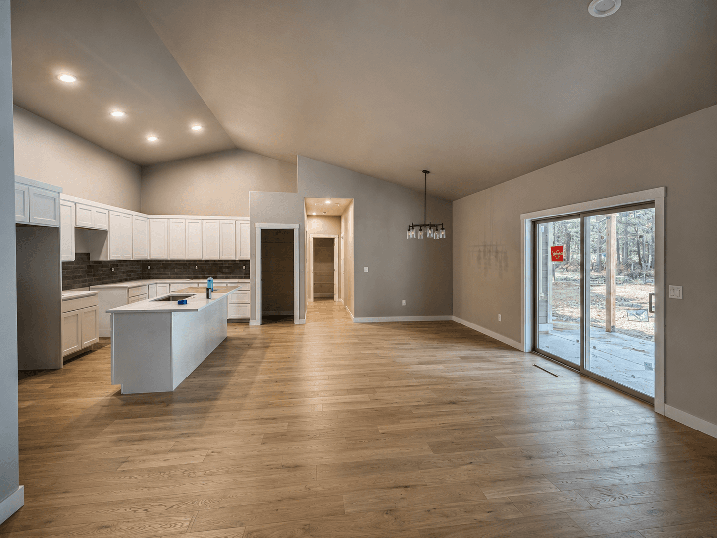 Modern open-concept interior featuring a white kitchen, light wood floors, and sliding glass doors.